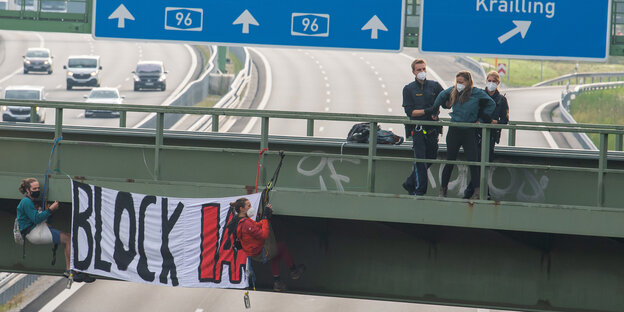 Eine Aktivistin, die an einer Banneraktion an einer Brücke über der Autobahn A96 bei Germering teilgenommen hat, wird abgeführt. Auf dem Banner steht „Block IAA“.