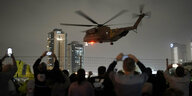 Ein Helikopter in der Nacht bei der Landung. Davor Menschen, die Fotos machen.