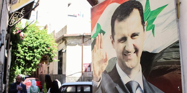 Ein Plakat hänt an einer Wand mit dem Bild des syrischen Präsidenten Bashar al-Assad der lächelnd winkt