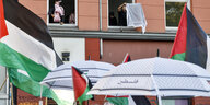 Männer halten Palästinensertücher aus den Fenstern während unten eine Demonstrationen mit Palästinenserfahnen auf der Straße vorbeiläuft