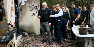 Steinmeier steht neben Präsident Herzog und anderen Menschen, alle in Schutzwesten auf Scherben neben einem Haus