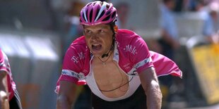 Jan Ullrich mit schmerzverzerrtem Gesicht und offenem Trikot beim Bergauffahren