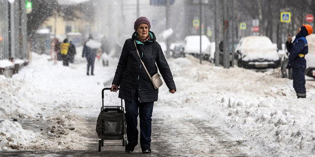 Moskau, der Schnee türmt sich auf dem Gehweg, auf dem eine Passantin einen Hackenporsche hinter sich her zieht