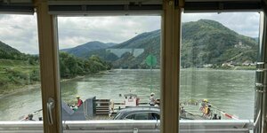 Blick durch ein Schiffsfenster einer Fähre auf einem Fluss mit Bergen