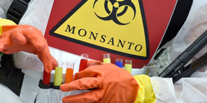 Handschuhe fassen Röhrchen mit buntem Pulver an, Schild mit der Aufschrift Monsanto