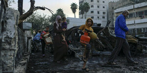 PalästinenserInnen tragen Habseligkeiten oder Kinder bei sich, als sie das Al-Ahli-Krankenhaus in Gaza-Stadt verlassen. Die Straße ist von verbrannten Autos und Bäumen gesäumt