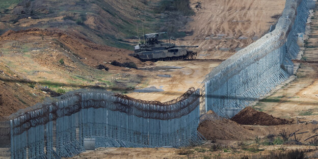 Ein isrelischer Panzer steht vor dem Grenzzaun zum Gazastreifen - die Erde ist aufgewühlt, der Panzer zielt Richtung Gaza