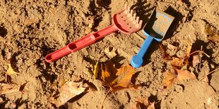 Sandspielzeug im Sand und ein herbstblatt