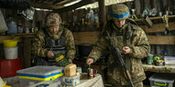 Zwei ukrainische Soldaten stehen in einem Unterstand und machen eine Pause, einer der Soldaten kocht Kaffee, der andere rührt beiläufig mit einem Löffel in der Tasse
