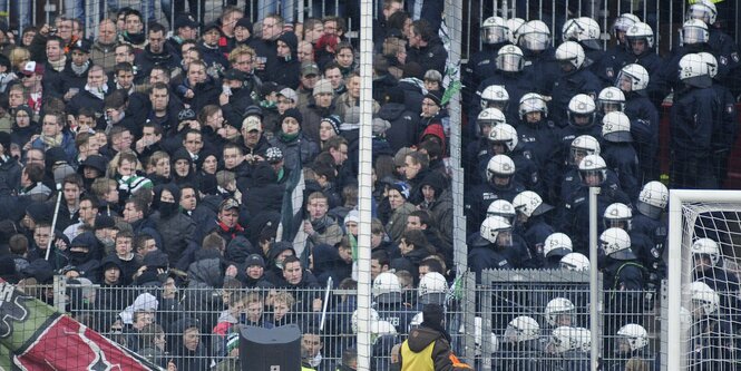 Fußballfans auf der linken Seite, behelmte Polizisten auf der rechten Seite