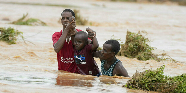Zwei Männer tragen ein Kind durch ein Hochwasser