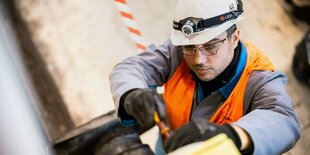 Ein Handwerker mit Bauhelm und Schutzweste schraubt etwas fest.