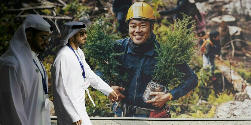 Zwei Männer in traditioneller Kleidung laufen einem Werbeplakat für die Klimakonferenz COP28 vorbei