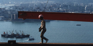 Ein Bauarbeiter mit Helm läuft auf einem Stahlträger über der Skyline von Hongkong