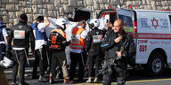 Bewaffnete Polizeibeamte sichern Rettungskräfte ab, die offenbar mit einem weißen Tuch abgeschirmt eine Person in einen Rettungswagen tragen