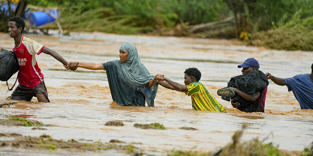 Menschen bilden eine Kette und versuchen gemeinsam eine überflutete Straße zu überqueren