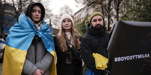 Vlada Urobiova mit ukrainischer Flagge um die Schultern, , Krista-Marija Läbe und Pavlo Melnyk, der ein Transparent hält: #BOYCOTTMILKA