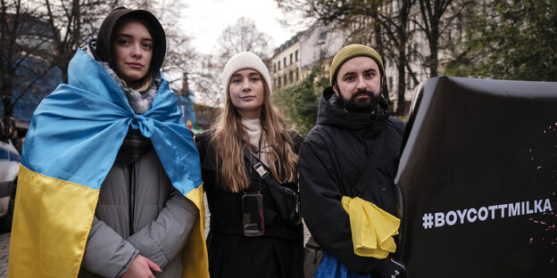 Vlada Urobiova mit ukrainischer Flagge um die Schultern, , Krista-Marija Läbe und Pavlo Melnyk, der ein Transparent hält: #BOYCOTTMILKA
