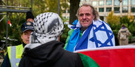 Im Vordergrund steht jemand mit einem Pali-Tuch und einer Pali-Fahne, ihm gegenüber ein Mann, der sich eine Israel-Fahne über die Schulter gehängt hat