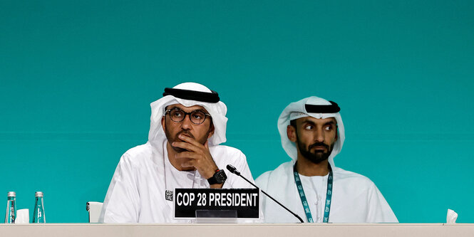 Zwei Männer in traditioneller Kleidung sitzen auf einem Podium