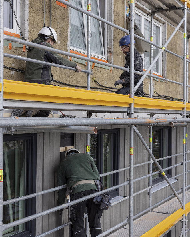 Bauarbeiter stehen auf dem Gerüst und montieren die Fertigteile an die Fassade