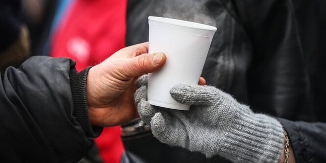 Eine Hand, die einen Handschuh trägt reicht einen Pappbecher mit dampfender Suppe weiter