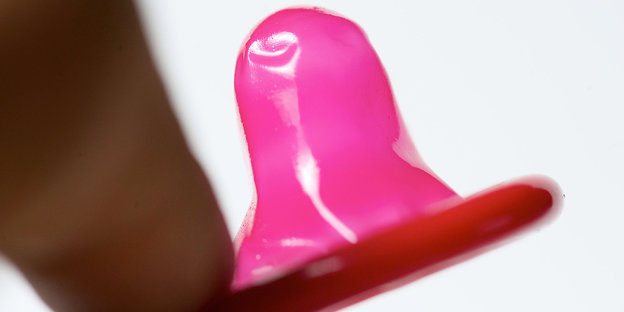 Zwei Finger halten ein zusammengerolltes Kondom.