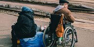 Ukraine-Flüchtling im Rollstuhl und alte Frau sitzend auf blauem Müllsack