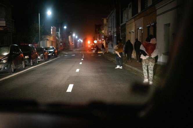 Menschen laufen im Scheinwerferlicht eines Autos auf der Straße einer Kleinstadt