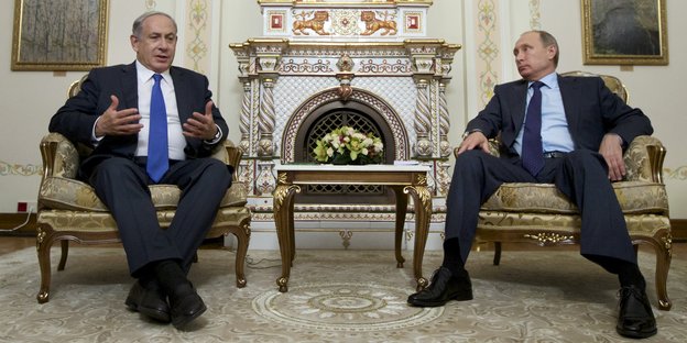 Putin und Netanjahu sitzen in einem Saal, im Hintergrund ein Ofen.