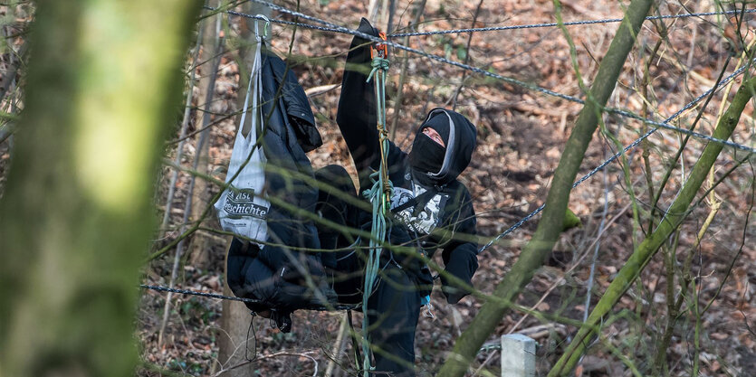 Ein vermummter Aktivist hängt an einem Seil im Baum