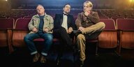 Drei Männer sitzen in einem Kinosaal nebeneinander