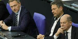 Olaf Scholz, Robert Habeck und Christian Lindner sitzen gemeinsam nebeneinander im Bundestag