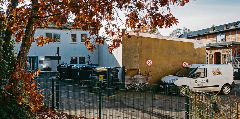 Ein weißes Auto vor einer Wand, dahinter ein weißes, zweistöckiges Gebäude