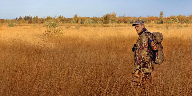 Ein Mann in Tarnkleidung steht inmitten trockener Gräser
