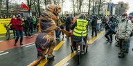 Ein Mensch, verkleidet als Dinosaurier, und Fahrradfahrer protestieren