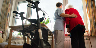 Eine Pflegerin steht mit einer älteren Person vor einem Fenster