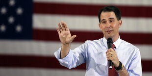 Scott Walker spricht vor US-Flagge und hebt die Hand