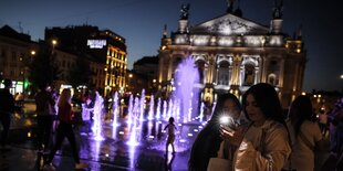 Frauen stehen mit Handys vor einem beleuchteten Gebäude