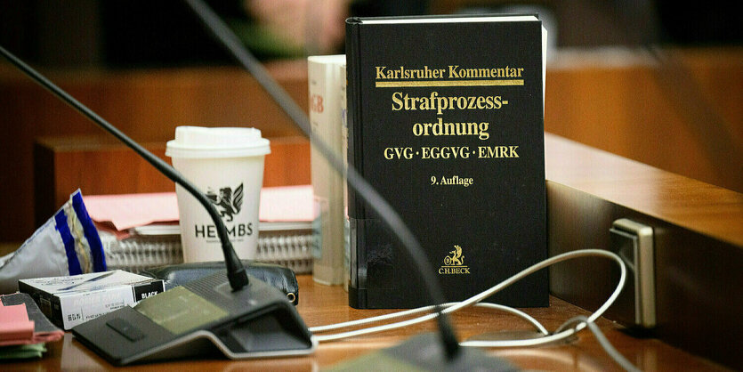 Auf einem Tisch sind verschiedene Akten und Bücher zu sehen, sowie zwei Mikrophone und ein Kaffebecher.