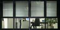 Eine Person sitzt hinter einem beleuchteten Bürofenster auf einem Stuhl hinter einem Bürofenster