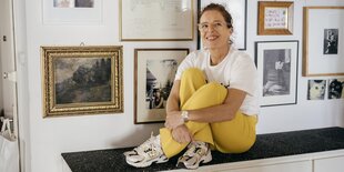 Sandra Schwittau sitzt auf einem Sideboard in ihrer Münchener Wohnung vor einer Bilderwand.