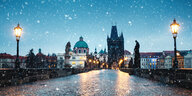 Laternen leuchten warm und Schnee fällt auf die Prager Karlsbrücke