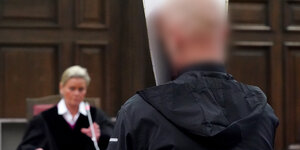 Ein Mann sitzt vor einer Richterin und verdeckt sein Gesicht