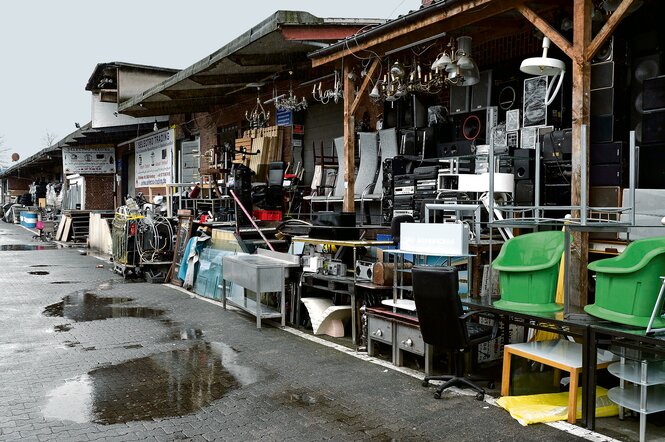 Elektrogeräte und andere Waren stehen vor einer Lagerhalle zum Verkauf.