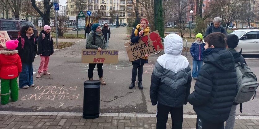 Eltern und Kinder halten Plakate hoch während eine Frau, die Forderungen des Protestes verkündet.