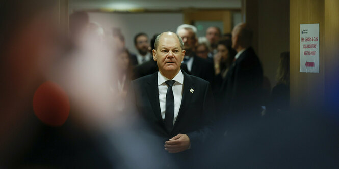 Olaf Scholz betritt eien Saal, im Hintergrund stehen Männer mit Anzügen