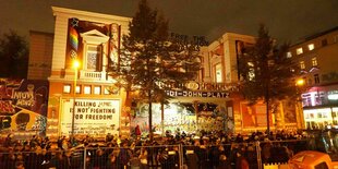 Teilnehmer einer Pro-Israel Demo stehen vor dem Gebäude der Roten Flora in Hamburg. An der angestrahlten Fassade hängt ein Transparent: Killing Humans is not fighting for freedom"