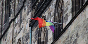 Regenbogenfahne ist aus dem Fenster eines Kirchenfensters gesteckt