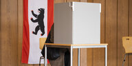 Das Bild zeigt eine Wahlkabine mit der Berliner Flagge im Hintergrund.